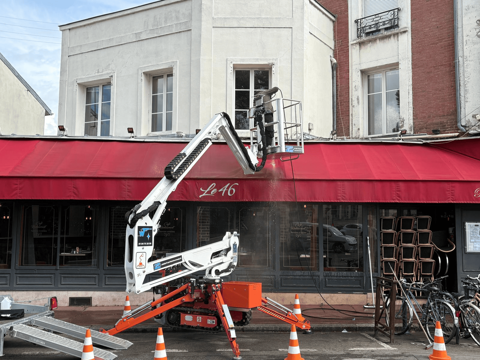 Lavage de store en hauteur avec nacelle -StoreWash Technicien StoreWash en nacelle en train de nettoyer un store banne en hauteur sur façade commerciale